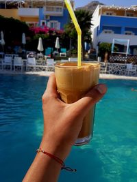 Close-up of hand holding drink by swimming pool