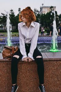 Young woman sitting on wall against fountain