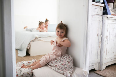 Funny toddler girl next to sisters, playing on laptop on bed. concept happy childhood and siblings, 