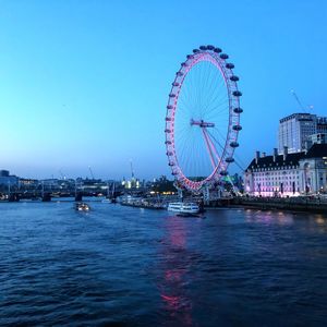 Ferris wheel by river in city against sky at dusk