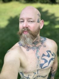 Portrait of shirtless man with tattoo standing in yard