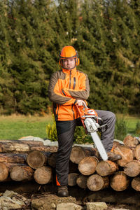 Full length of man holding chainsaw while standing against logs