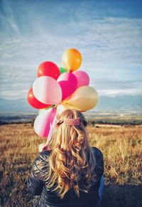 Rear view of woman with balloons standing on field