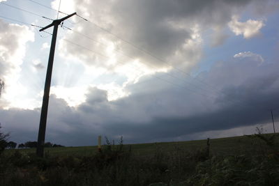 Electricity pylon on field against cloudy sky