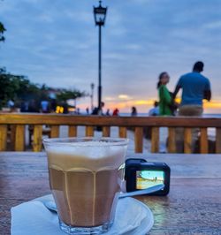 Close-up of coffee cup while couple standing in background against sky