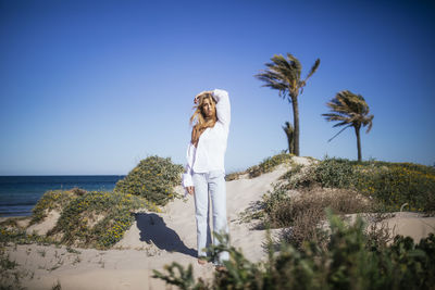 Beautiful blonde young woman standing at beach in a sunny day with urban clothes