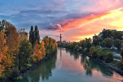 River amidst trees and buildings against sky during sunset