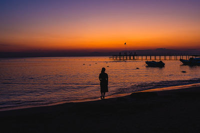 Silhouette man standing on beach against sky during sunset