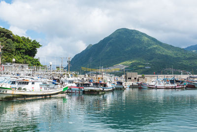 Sailboats moored on sea by mountains against sky