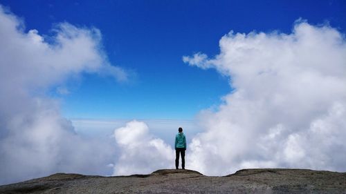 Rear view of female hiker standing on rocky peak against sky