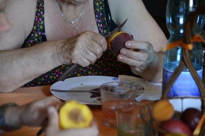 Midsection of senior woman cutting plum on table at home