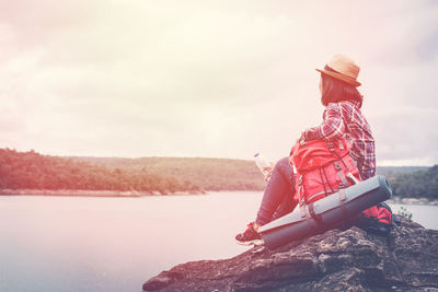 Side view of woman with backpack sitting on rock by lake