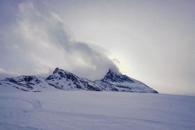 Scenic view of snow covered mountains against cloudy sky