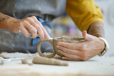 Ceramist hands shaping ceramic cup of raw clay material using professional potter tools in workshop