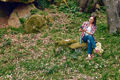 Woman sitting in forest on a stone, using mobile phone for chat or looking for gps. traveling. 