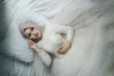 Asian muslim bride in white wedding gown with hijab or jilbab lying on bed. bridal wedding concept