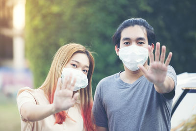 Young asia couple in protective masks showing stop gesture at garden home person