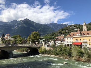 Bridge over river by buildings against sky