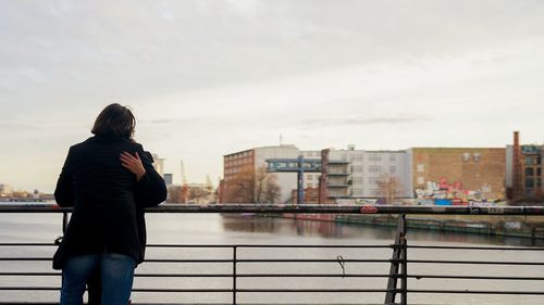 Rear view of woman standing by railing against sky