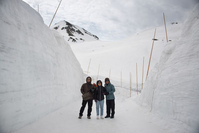 Friends standing on snow covered 0field against sky