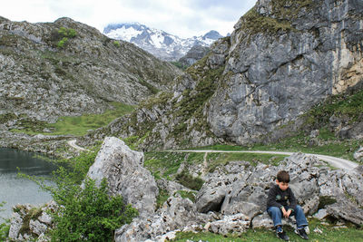 Boy sitting on rock against mountains