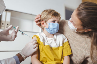 Boy getting vaccinated by doctor with mother at center