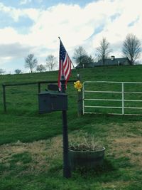Bare trees on field against cloudy sky
