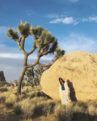 Woman standing by rock formation and trees on field against sky