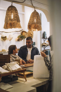 Father and daughter looking at each other while saleswoman packing bag in store