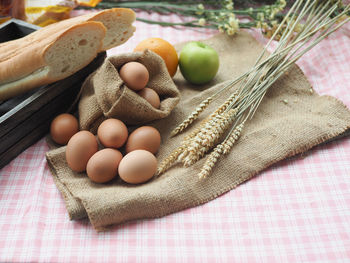 Baguettes, eggs, wheat, apple and orage on brown sackcloth on pink tablecloth with copy space.