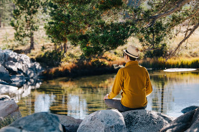 Man sitting on the rock near the peaceful small lake at early fall day. 
