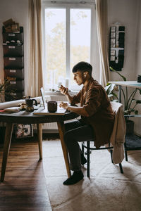 Male business professional talking through speaker phone and using laptop at home office