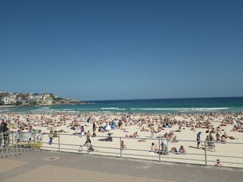 People enjoying at beach against clear blue sky