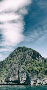 Scenic view of sea by mountain against sky