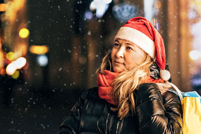 Portrait of a woman in a santa hat with christmas shopping in colorful bags on the street decorated