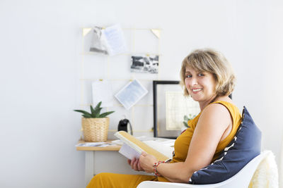 Portrait of smiling woman reading book sitting at home