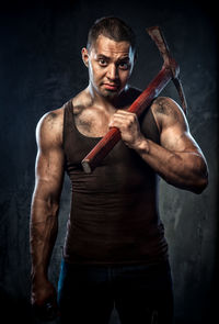 Portrait of muscular man holding pick axe against wall