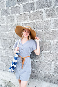 Portrait of smiling young woman standing against wall