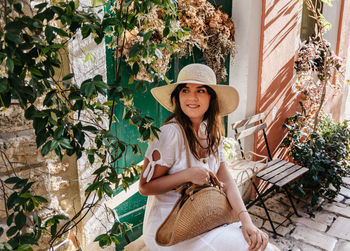 Portrait of happy young woman wearing stylish summer clothes, sitting in street of idyllic old town