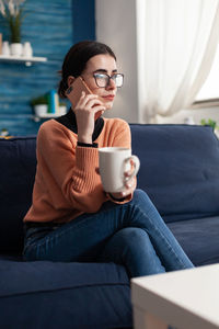 Young woman talking on phone while sitting on sofa at home