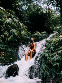 Young man in river amidst trees in forest