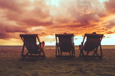 Chairs on beach against sky during sunset