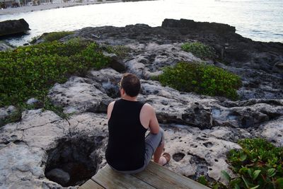 Rear view of man sitting on rock by sea