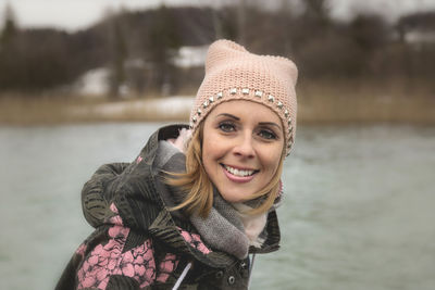 Portrait of woman smiling while standing against lake during winter