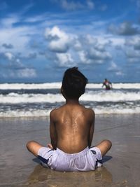 Rear view of shirtless man sitting on beach