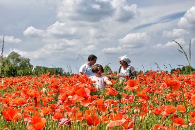 Low angle view of people on flowering plants on field against sky