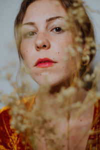 Close-up portrait of young woman seen through dried plant