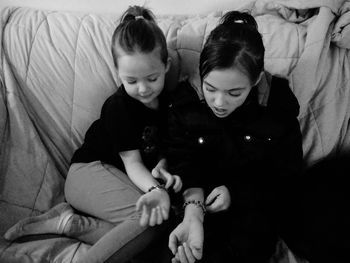 High angle view of sisters wearing bracelets while sitting on sofa at home