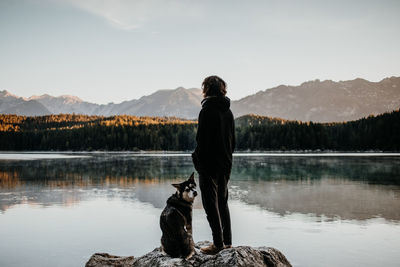 Man with dog standing at lakeshore against sky