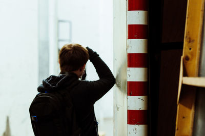 Rear view of man wearing backpack while standing by wall